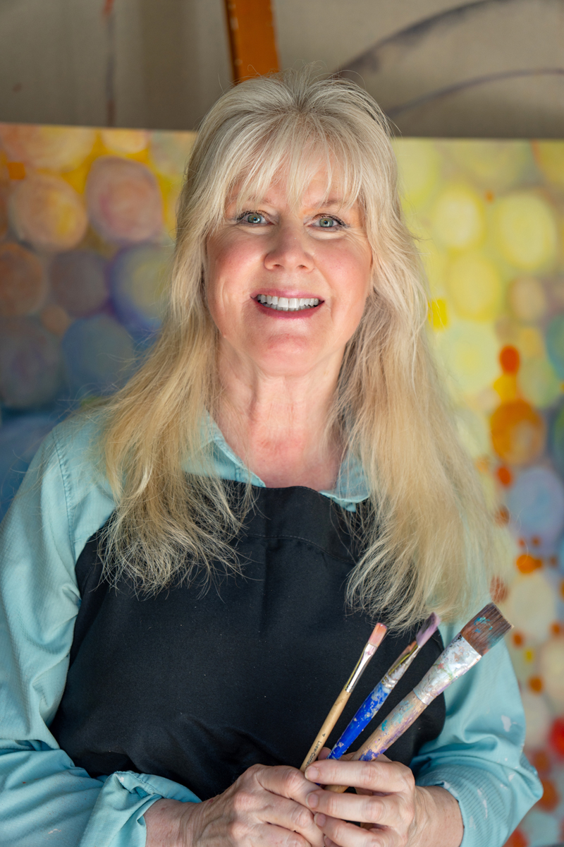 Trisha Selgrath, fine artist and creator of MovingAbstracts interactive wall art, in her studio holding paintbrushes